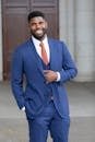 Smiling businessman in a blue suit posing comfortably outdoors with an elegant demeanor.